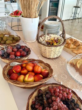 İçinde şeftali, üzüm, erik ve kruvasan, hamur işi ve pasta bulunan sepetler dolusu taze meyve dolu güzel bir brunch masası..