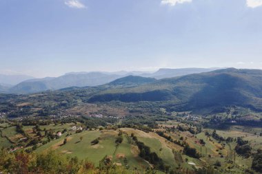 Tepesinde mavi gökyüzü olan yeşil bir vadide yuva yapmış dağlık bir köyün panoramik manzarası.