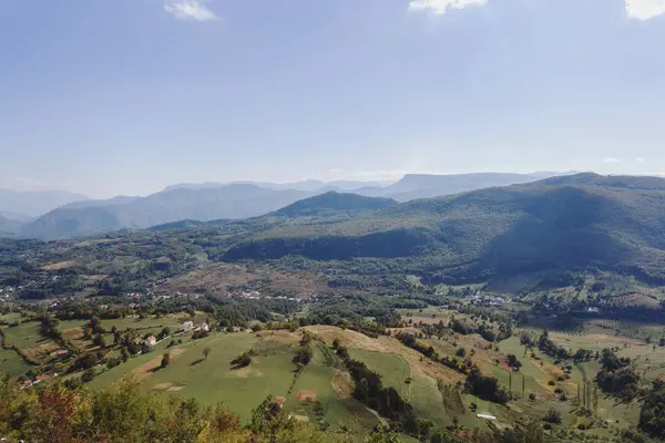 Tepesinde mavi gökyüzü olan yeşil bir vadide yuva yapmış dağlık bir köyün panoramik manzarası.