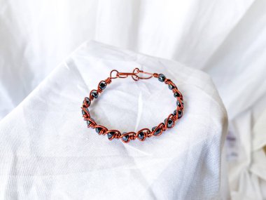 Metalik boncuklu el yapımı bakır bilezik. Kabloya sarılı aksesuarlar, beyaz arkaplan.