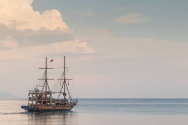 Gün batımında sakin bir okyanusta gezinen heybetli, uzun bir gemi çarpıcı bir gökyüzü ve ufukla çevrili macera ve huzur hissi uyandırıyor. Alanya Şehir Limanı.