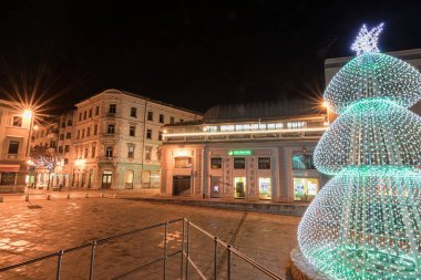 An ancient stone arch and nearby structures brightly light up with festive decorations at night, creating a magical holiday atmosphere and stunning architectural contrasts. Golden door, Pula. clipart