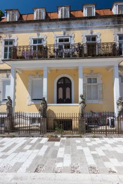 Zarif mimarinin, karmaşık balkonların ve taş heykellerin sergilendiği tarihi sarı bina, manzaralı kentsel bir ortamda kültürel ve mimari mirası vurguluyor..