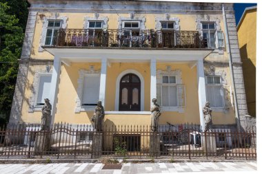 Historic yellow building showcasing elegant architecture, intricate balconies, and stone statues, emphasizing cultural and architectural heritage amidst a scenic urban environment. clipart