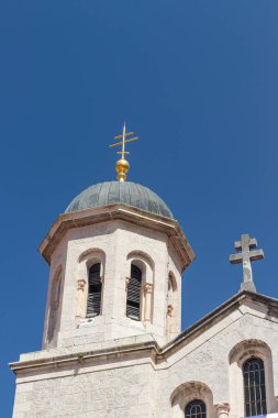 Taş işçiliği ve çan kuleleri olan geleneksel bir kilise parlak mavi gökyüzüne karşı görülüyor. Mimari ayrıntılar ve uyumlu tasarım tarihi ve kültürel önemi yansıtır..