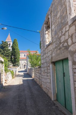 Idyllic kırsal kesimde, canlı mavi gökyüzünün altında yeşil ile çevrili bir kilise kulesinin bulunduğu taştan yapılmış büyüleyici bir köy sergileniyor..