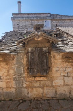 Parlak mavi gökyüzünün altında yıpranmış ahşap panjurlar ve tahta bir çatı barındıran taştan bir binanın büyüleyici manzarası tarih ve geleneksel zanaatkarlığı çağrıştırıyor..