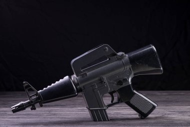 Siyah arkaplana karşı ahşap bir yüzeye yerleştirilmiş koyu metalik bir oyuncak silah. Detaylı işçilik ve stüdyo ışıklandırması içeriyor..
