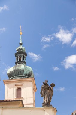 Tarihi bir kilise kulesinin çarpıcı tasviri. Dekoratif bir kubbe ve canlı mavi gökyüzünün altında dinsel bir heykel. Mimari zarafet ve kültür mirasını yansıtıyor..