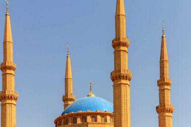 Mavi kubbeler ve parlak mavi gökyüzü altında altın minareler bulunan bir caminin çarpıcı bir mimari görüntüsü. Yapıda geleneksel İslami tasarım ilkelerinin karmaşık ayrıntıları yer alıyor.