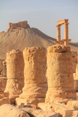 Uzaktaki bir tepenin tepesinde yer alan tarihi bir arkeoloji sahasındaki antik taş sütunların bir görüntüsü. Sahne ebedi güzellik ve tarihsel önemi taşır..
