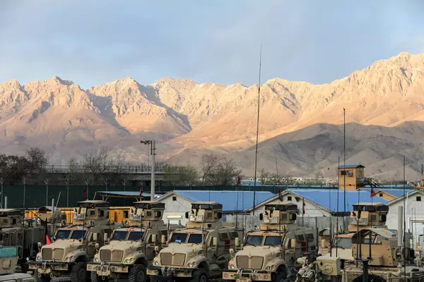 Birkaç zırhlı araçla donatılmış bir askeri kamp berrak bir gökyüzünün altında çarpıcı bir dağın önüne kurulur..