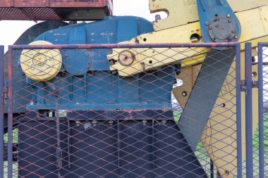 Renkli endüstriyel makineler, vites, metal yapı ve işlevsel bir tasarım, güvenlik çitlerinden bakılıyor, mühendislik ve imalat teknolojilerini sembolize ediyor.