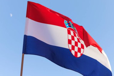 Canlı Hırvat bayrağı açık mavi gökyüzünün altında, ulusal gurur ve kültür mirasını sembolize eden belirgin kırmızı ve beyaz amblemini sergileyerek dalgalanıyor..