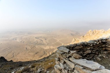 Yumuşak mavi bir gökyüzünün altında geniş bir manzaraya bakan kayalık bir yamaçtan büyüleyici bir manzara. Uzak arazi sisli bir ufuk oluşturuyor. Huzur ve macera hissi uyandırıyor..
