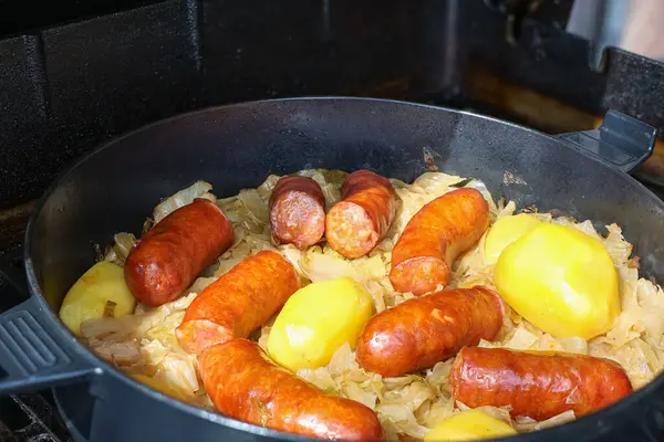 Lezzetli sosisler, bütün patatesler ve pişirilmiş lahanalarla dolu otantik ve doyurucu bir yemek için bir tavada birlikte hazırlanmış..
