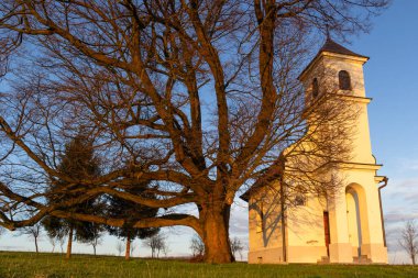 Sakin bir taşra kilisesi, günbatımının ılık parıltısının altında büyük olgun bir ağacın yanında oturur. Geniş doğal güzelliklerle çevrili sakin ve resmedilmiş bir atmosferi anımsatır..
