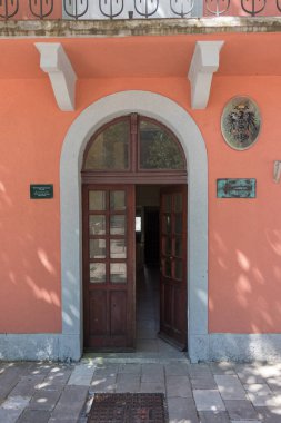 CETINJE, MONTENEGRO, 06.25.2019: Şeftali renkli bir binanın kemerli ahşap kapısının, geleneksel mimari detayları, dış ışık yansımaları ve gölgelere karşı kontrastlı, samimi ve davetkar bir ortam için.