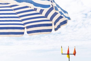 ALANA, TURKEY, 10.08.2018: Mavi çizgili plaj şemsiyesi güneşli ve parlak bir gökyüzü altında gölge ve işaret bayrakları vererek, rahatlatıcı bir yaz hissi uyandırıyor. Plaj, tatil ve seyahatle ilgili konular için harika.