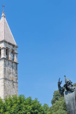 BÖLÜM, CROATIA, 08.06.2018: Kültürel ve tarihsel önemi çağrıştıran açık mavi gökyüzünün altında, yemyeşil bir yeşil ile çevrili tarihi bir çan kulesinin bulunduğu sakin bir sahne.