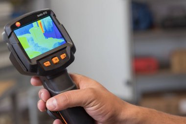 VINKOVCI, CROATIA, 06.20.2018: Bir odada ısı izi yakalamak için bir termal görüntüleme cihazı tutmak, ısı tanılama, enerji verimliliği ve sıcak noktaları tanımlamak için kullanılan teknolojiyi göstermek.