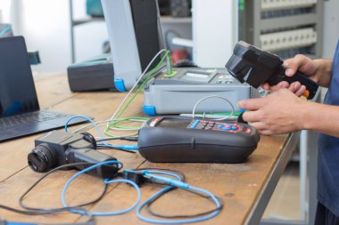 VINKOVCI, CROATIA, 06.20.2018: Tahta bir masada çeşitli elektronik aletlerle çevrili test ekipmanlarıyla çalışan teknisyen. Kurulumda modern hassas cihazlarla profesyonel bir teknoloji ve mühendislik ortamı sergileniyor..