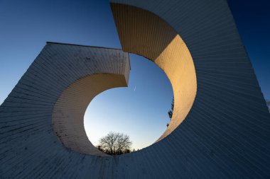 NOVA GORICA, CROATIA, 03.18.2020: Çembersel bir tasarıma sahip modern beyaz beton anıt, kaldırım taşlarının arasında, berrak mavi bir gökyüzünün altında yeşil çevreye sahip huzurlu bir semtte sergileniyor..