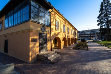 VELIKA GORICA, CROATIA, 03.18.2025: Büyük cam pencereler, dokulu duvarlar ve parlak güneş ışığı gösteren zarif tarihi bina. Klasik mimari detaylar ve sıcak bir atmosfer, kentsel env 'de tarihi ve kültürü sembolize ediyor.