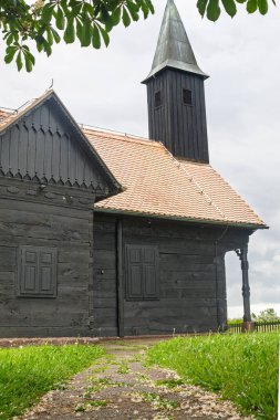 Gri, bulutlu bir gökyüzünün altında yeşil çimlerle çevrili önemli bir çan kulesinin bulunduğu tarihi ahşap bir şapel..