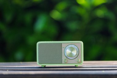 VINKOVCI, CROATIA, 06.13.2025: Ahşap bir masada dinlenen, yemyeşil, bulanık yeşil arka planlı, barışçıl ve nostaljik bir ortam yaratan, antika yeşil bir radyonun yakın plan çekimi.