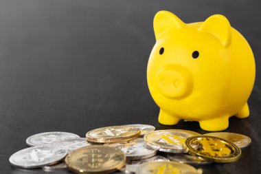 Sarı kumbaranın etrafı gümüş ve altın Bitcoin paralarla çevrili gri bir yüzey. Görüntü, modern teknoloji güdümlü bankacılık sektöründeki dijital para birimi, mali tasarruf ve yatırım stratejilerini sembolize ediyor..