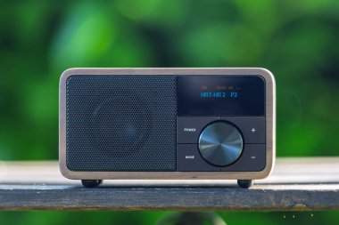 VINKOVCI, CROATIA, 06.13.2025: Ahşap bir masada dinlenen, yemyeşil, bulanık yeşil arka planlı, barışçıl ve nostaljik bir ortam yaratan, antika yeşil bir radyonun yakın plan çekimi.