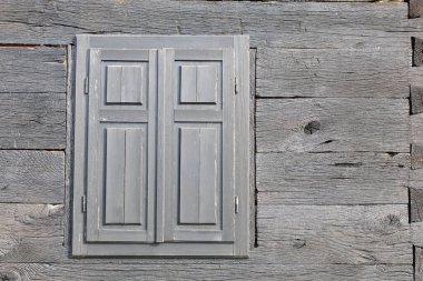 Kırsal ahşap duvar canlı bir dokuya ve kapalı panjurlara sahip büyüleyici basitliği ve ahşap işçiliğin zarafetini vurguluyor..