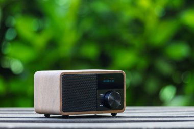 VINKOVCI, CROATIA, 06.13.2025: Ahşap bir masada dinlenen, yemyeşil, bulanık yeşil arka planlı, barışçıl ve nostaljik bir ortam yaratan, antika yeşil bir radyonun yakın plan çekimi.