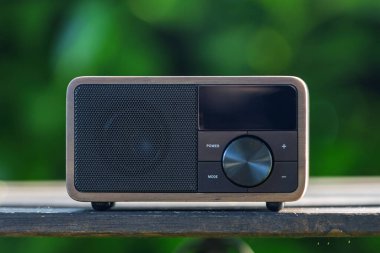 VINKOVCI, CROATIA, 06.13.2025: Ahşap bir masada dinlenen, yemyeşil, bulanık yeşil arka planlı, barışçıl ve nostaljik bir ortam yaratan, antika yeşil bir radyonun yakın plan çekimi.