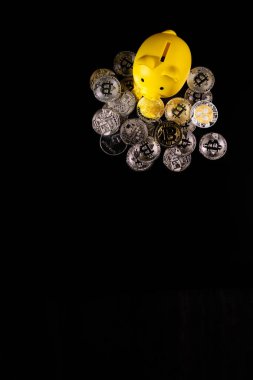 Siyah bir yüzey üzerinde gümüş ve altın Bitcoin paralarla çevrili sarı bir kumbara. Görüntü, modern teknoloji güdümlü bankacılık sektöründeki dijital para birimi, mali tasarruf ve yatırım stratejilerini sembolize ediyor..