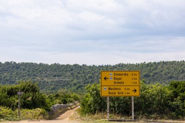 Hırvatistan 'ın huzurlu bir kırsalında, Stomorska, Rogac, Grohote, Maslinica ve Donje Selo' yu gösteren parlak sarı bir yol işareti bulunuyor. Yuvarlanan tepeler ve kirli bir patika Sakin bir seyahat sahnesi oluşturur.