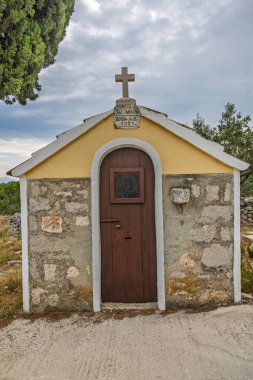 Sarı bukleli ve kırmızı kiremitli küçük bir taş şapel, güneşte pişirilmiş kırsal bir alanda, selvi çiçeğinin yanında yer alır. Sahne, dinginliği, yalnızlığı ve kırsal cazibeyi yansıtıyor..