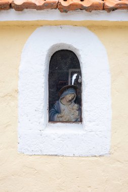 Bebek İsa 'nın soluk sarı bir duvarda kemerli bir pencerede oturduğu küçük bir dini resim. Sıcak, özverili, eski mimari detaylarıyla kilisevari bir cazibe..