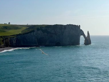 Etretat kayalıklarının panoramik manzarası, Normandiya, Fransa. Mavi denize karşı belirgin bir doğal kemer görünür. Uçurumlar dik, dikey yapıları ve kayalık dokusuyla karakterize edilir.. 