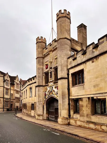 Cambridge Üniversitesi Büyük Kapısı, Cambridge, Birleşik Krallık. Soluk taştan yapılmış, siperli kuleleri olan sağlam kemerli bir kapı, ağır ahşap kapılarının üzerinde karmaşık armaklar sergiliyor.. 