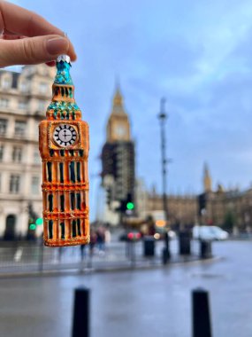 Big Ben Kulesi şeklinde Noel ağacı süsü. Elinde Big Ben 'e benzeyen bir süs var. Üzerinde mavi ve altın renkleri var.. 