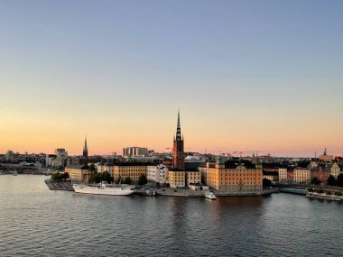 İsveç 'in eski Stockholm kentinin panoraması. Limanı olan tarihi bir bölgenin şehir manzarası. Ön plandaki su, akşam gökyüzünün yumuşak renklerini yansıtır.. 