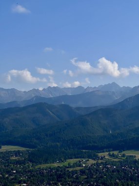 Polonya 'nın Zakopane kentindeki Tatra dağlarının panoramik manzarası. Dağılmış bulutlu açık mavi bir gökyüzü dağlık arkaplanı güçlendirir.. 