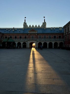 Lublin Kalesi 'nin kapıları gün batımında Polonya geçitleri, alçak güneş ışığıyla aydınlanan bir yol yaratıyor ve taş kaldırım işçilerine uzun bir altın yansıma yapıyor.