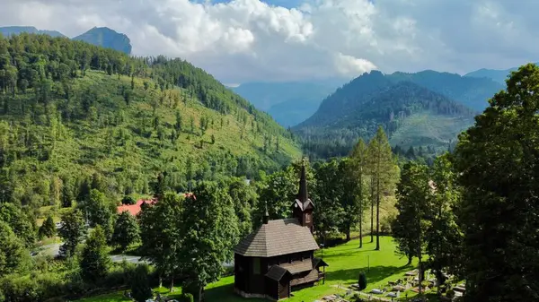 Slovakya 'nın Tatranska Javorina kentindeki kilisenin ve Tatra dağlarının çarpıcı panoramik manzarası. Yoğun orman ve yuvarlanan tepelerle çevrili yemyeşil vadide yuva yapmış ahşap kilise.