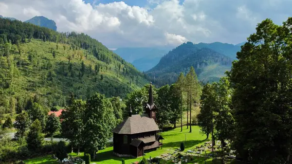 Slovakya 'nın Tatranska Javorina kentindeki kilisenin ve Tatra dağlarının çarpıcı panoramik manzarası. Yoğun orman ve yuvarlanan tepelerle çevrili yemyeşil vadide yuva yapmış ahşap kilise.