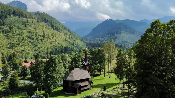 Slovakya 'nın Tatranska Javorina kentindeki kilisenin ve Tatra dağlarının çarpıcı panoramik manzarası. Yoğun orman ve yuvarlanan tepelerle çevrili yemyeşil vadide yuva yapmış ahşap kilise.