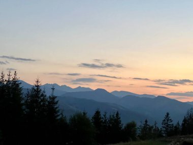 Tatra dağlarında gün batımı, Zakopane, Polonya. Karanlık, sivri dağ siluetleri yumuşak portakallar ve mavilerden oluşan solgun bir gökyüzüne karşı yükseliyor.. 