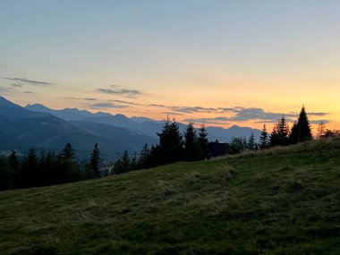 Tatra dağlarında gün batımı, Zakopane, Polonya. Karanlık, sivri dağ siluetleri yumuşak portakallar ve mavilerden oluşan solgun bir gökyüzüne karşı yükseliyor.. 